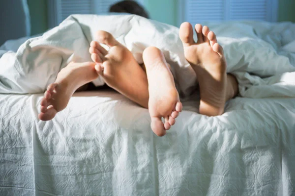Imagem colorida dos pés de um casal na cama