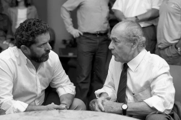 homem de barba e homem mais velho usando camisas sociais conversam em foto preto e branco