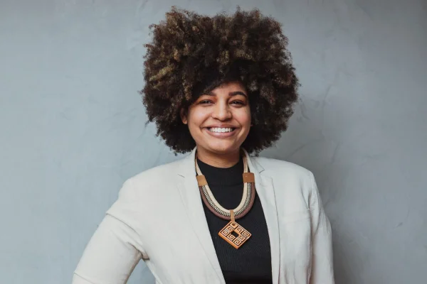 Fotografia colorida da jornalista Milena Teixeira, que veste um blazer branco sobre uma blusa preta