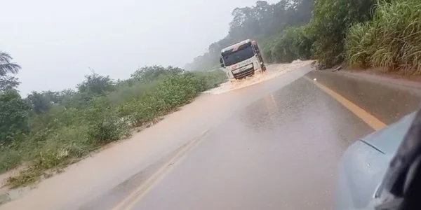 Imagem colorida de caminhão passando em pista de rodovia alagada - Metrópoles