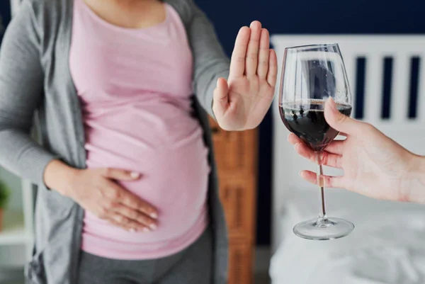 Foto colorida de mulher grávida com uma mão na barriga e a outra empurrando taça de vinho consumo de álcool na gravidez - Metrópoles