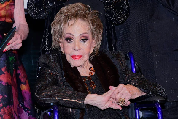foto colorida de mulher idosa de terno preto sentada em cadeira de rodas. Ela tem cabelos curtos e loiros e está maquiada - metrópoles