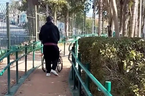 Imagens coloridas mostram homem, de costas, trajando conjunto de moletom na cor preta, empurrando uma cadeira de rodas em um parque
