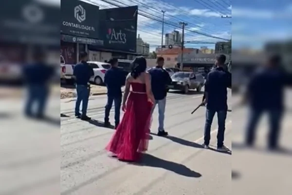 Mulher de vestido vermelho, de costas, e homens armados em pista