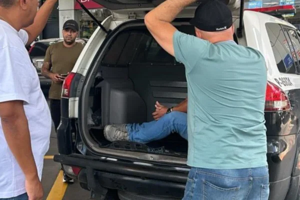 Imagem colorida de policial fechando porta-malas de viatura, com preso dentro - Metrópoles