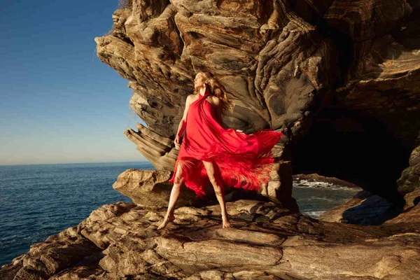 Na imagem com cor, uma mulher branca loira em uma rocha com um vestido vermelho - Metrópoles