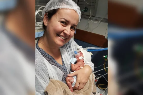 Foto colorida de mãe csegurando filho prematuro dentro de uma Unidade de Terapia Intensiva Neonatal - Metrópoles.