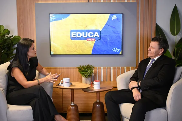 Vanessa e Veloso conversam frente a frente no estúdio, com o telão azul do Educa Talks exibindo o nome do programa ao fundo.