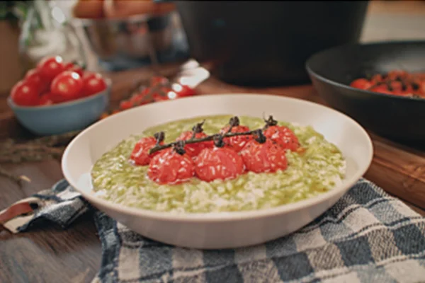 Na foto temos um prato com risoto verde e tomates confitados no meio