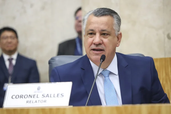 Imagem colorida mostra Coronel Salles, ex-PM, homem branco, grisalho, de terno azul escuro e gravata azul clara, sentado e falando ao microfone - Metrópoles