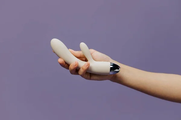 Foto colorida de uma mão feminina segurando um vibrador branco em um fudno roxo - Metrópoles