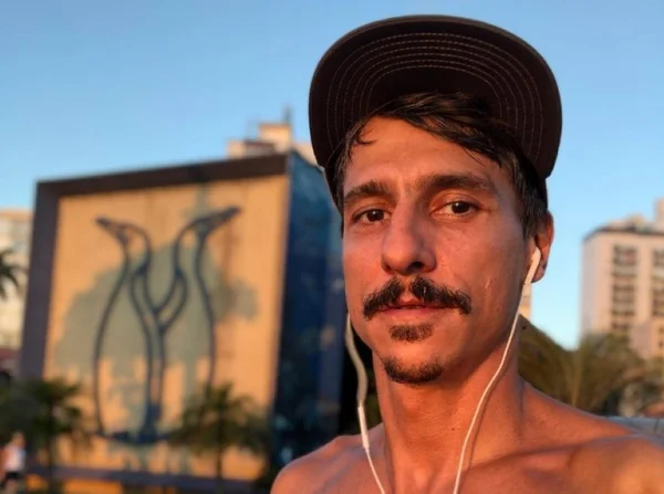 Gustavo Fildzz em foto colorida, de boné, sem camisa, fone de ouvido, de bigode