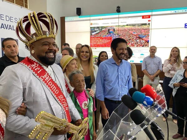 Imagem colorida mostra Ricardo Nunes, de camisa azul, com o rei momo do Carnaval e outras pessoas - Metrópoles