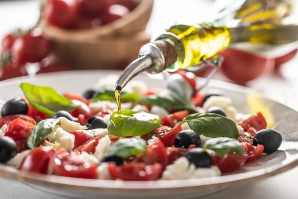 Imagem mostra pessoa colocando óleo em uma salada de tomate, rúcula e mussarela - Metrópoles - dieta