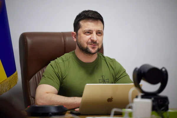 Presidente da Ucrânia, Volodymir Zelensky, durante conferência virtual. Ele está sentado diante de uma mesa e usa um notebook, sorrindo- Metrópoles