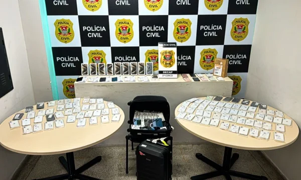 Celulares apreendidos divididos em duas mesas com o fundo da Polícia Civil
