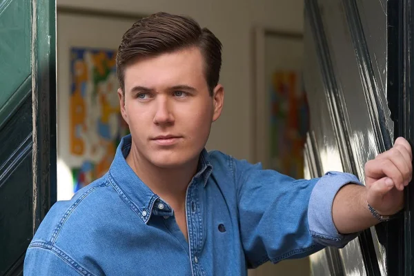 Foto colorida de homem com blusa azul perto de quadros - Metrópoles