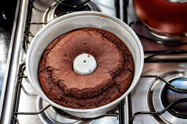 Imagem colorida mostra bolo de chocolate em uma forma em cima de um fogão - Metrópoles