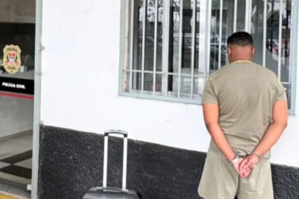 Imagem colorida de homem algemado de costas com mala do lado. Metrópoles