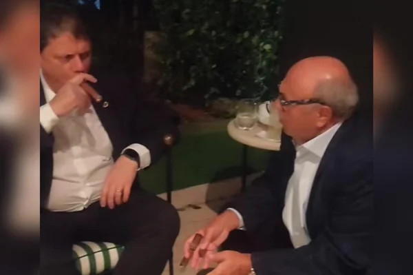 O ministro da Infraestrutura, Tarcísio de Freitas, fuma um charuto ao lado do empresário Washington Cinel, da Gocil - Metrópoles