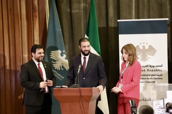Imagem colorida do presidente sírio Ahmed al-Sharaa se dirige ao povo enquanto acompanha e recebe informações do oficial eleitoral durante o processo eleitoral para a Assembleia Popular-Metrópoles