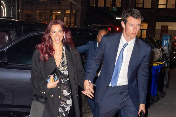 Imagem colorida de Dua Lipa e Callum Turner. Ele usa terno azul e ela, vestido preto - Metrópoles