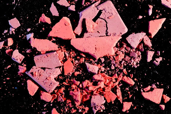 A imagem, com fundo preto, mostra restos de pó compacto e blush quebrados