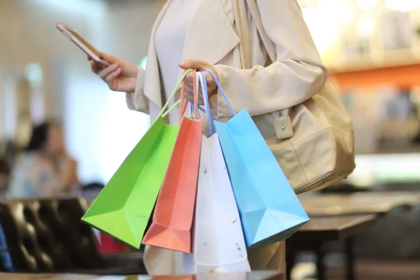 Foto colorida de mulher segurando sacolas em um shopping - Metrópoles.
