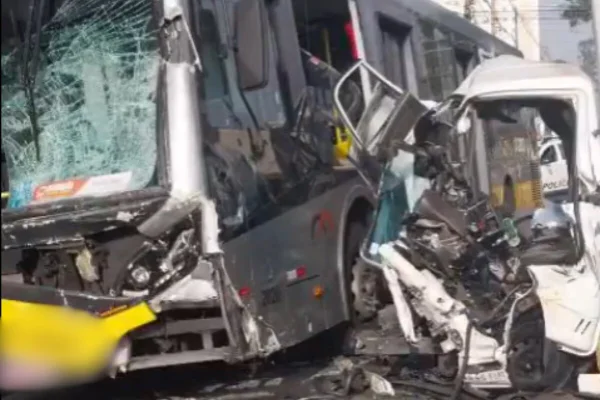 Foto colorida de ônibus amarelo e caminhão, com cabine destruída encostada no coletivo - Metrópoles