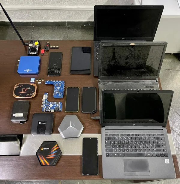 Imagem colorida mostra três notebooks, alguns aparelhos celulares e placas de computadores apreendidos durante operação policial contra a pedofilia - Metrópoles