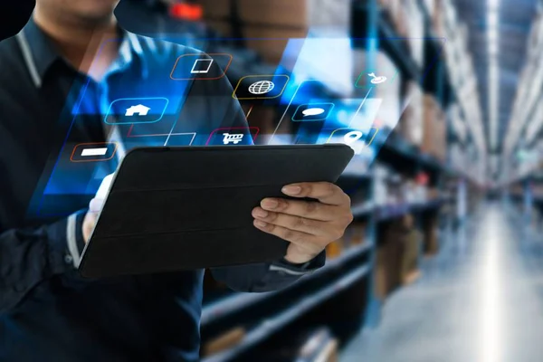 Homem usa tablet e hologramas com ícones aparecem frente à tela. Em fundo desfocado, corredor de estoque de loja - Metrópoles