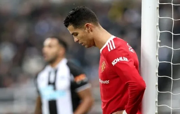 Na imagem colorida, um homem está posicionado no centro. Ele tem cabelos curtos, escuros, está usando uniforme de time de futebol e olha seriamente para a frente