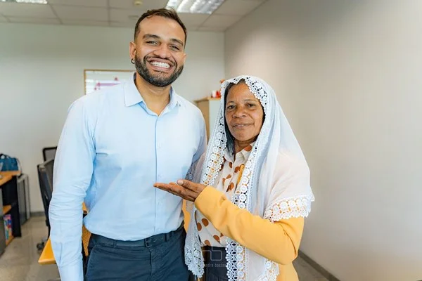 Fotografia colorida mostra homem de camisa azul sorrindo ao lado de mulher de véu branco