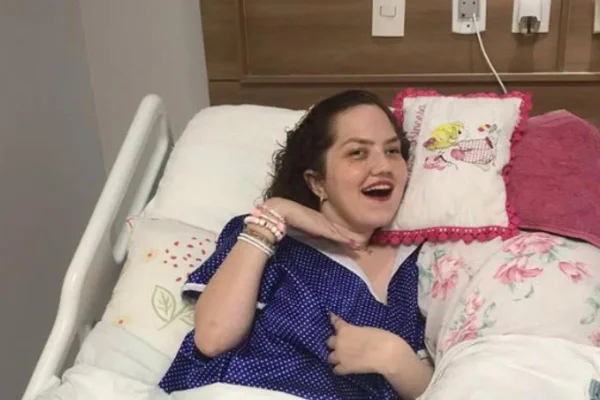 Foto colorida de mulher jovem posando em uma cama de hospital - Metrópoles.