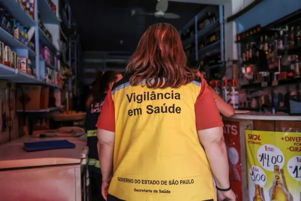 Imagem colorida de funcionária da Vigilância Sanitária de costas. Metrópoles