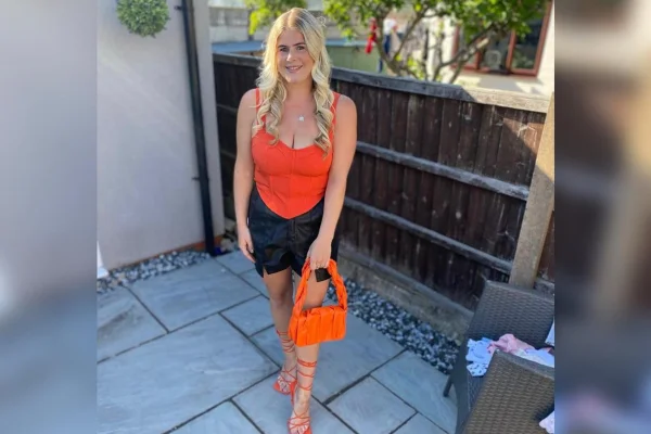 Foto de Emma Snape, uma mulher branca e loira, que está usando uma blusa laranja e um short jeans. Ela também segura uma bolsa laranja na mão esquerda - Metrópoles