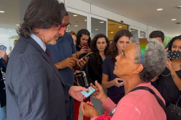 Imagem colorida mostra mulher entregando um bilhete ao fotógrafo Ricardo Stuckert na frente de hospital onde Lula está internado - Metrópoles