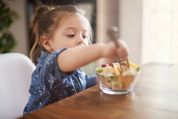 Imagem colorida de criança se alimentando com frutas - Metrópoles
