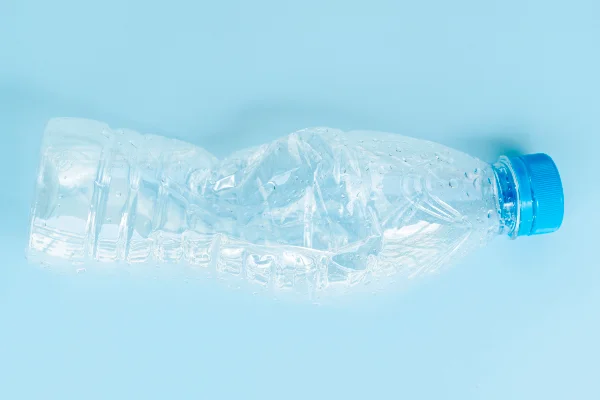 Foto colorida com fundo azul claro de garrafa pet amassada - METRÓPOLES.
