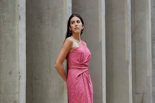 Modelo branca em pose de lado com vestido rosa em fundo de cimento queimado - Metrópoles