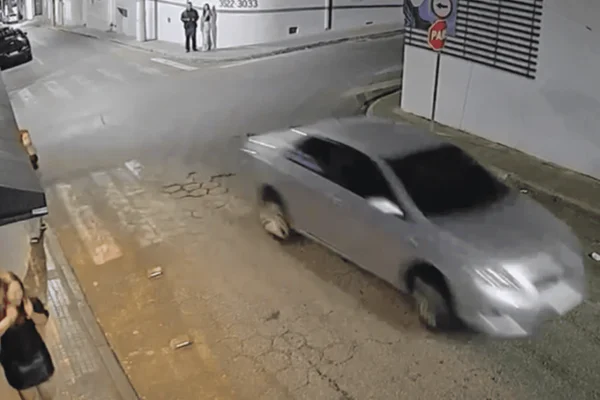 Imagem colorida de uma câmera de segurança mostra um carro cinza em alta velocidade e uma mulher com cara de assustada - Metrópoles