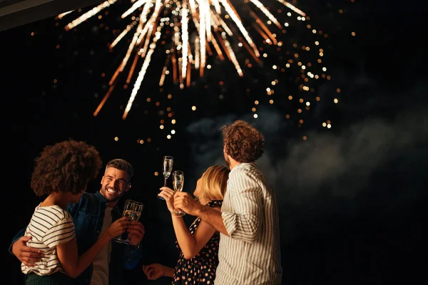 Grupo de quatro amigos. Eles estão com taça na mão e olham a queima de fogos de artifício