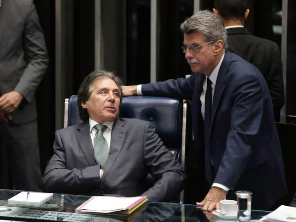 O ex-presidente do Senado, Eunício Oliveira, sentado, e o ex-senador Romero Jucá, de pé. Ambos conversam na mesa diretora do plenário da casa - Metrópoles