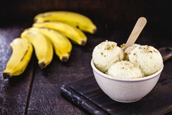 Sorvete de banana em um pote branco com bananas (frutas) ao fundo