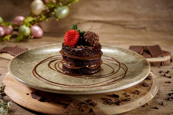 na foto vemos um prato com circulos de chocolate e uma torta de chocolate com morango em cima