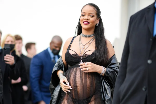 Cantora Rihanna na entrada do desfile da Dior. Ela está grávida e usa uma lingerie preta e um vestido de renda transparente por cima.