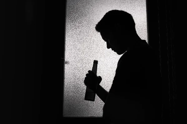 Foto preto e branco de uma silhueta masculina segurando uma garrafa de cabeça abaixada - Metrópoles.