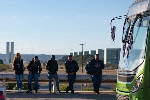 Foto colorida de pessoas de roupa de frio esperando ônibus em Brasília