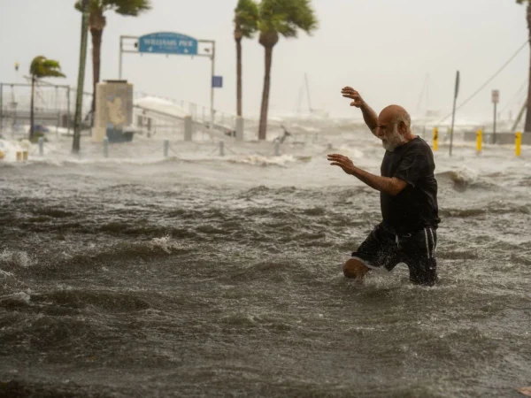 Foto colorida de homem atravessando área inundada por uma tempestade causada pelo furacão Helene, na costa de Gulfport, Flórida - Metrópoles