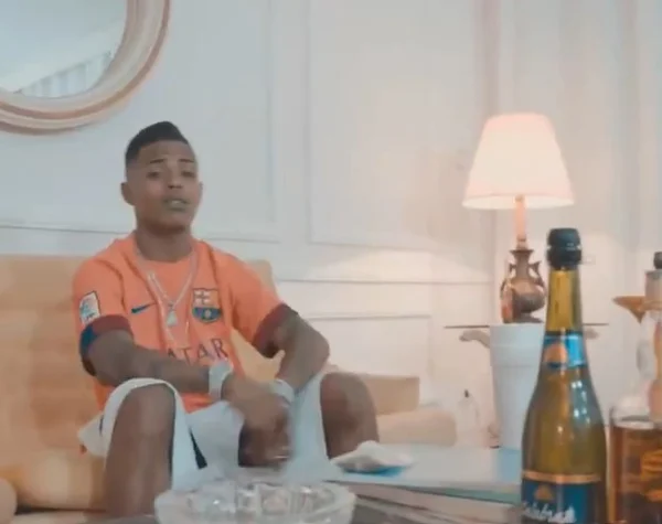 Imagem colorida mostra o rapper LK Metralha, um homem negro, vestido com uma camisa do Barcelona na cor salmão - Metrópoles